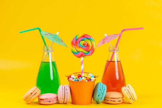 A front view drinks and macarons colorful and delicious along with lollipops and candies on yellow