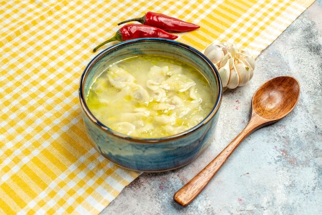 Front view dushbara dumplings soup in a bowl hot peppers garlic on yellow and white checkered kitchen towel wooden spoon on nude background food