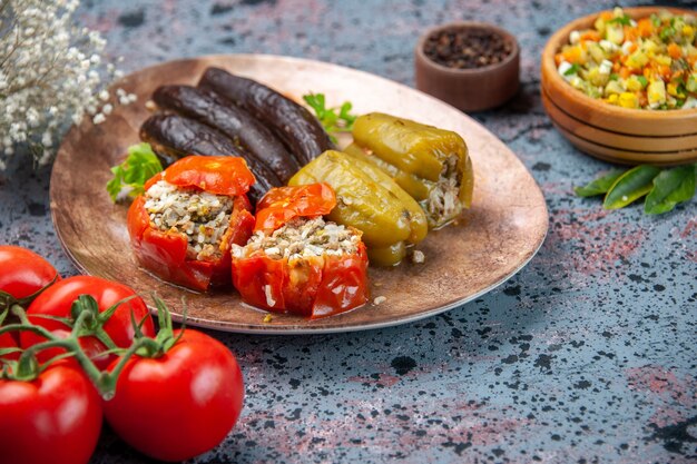 front view eggplant dolma with cooked tomatoes and bell-peppers filled with ground meat inside plate on blue background