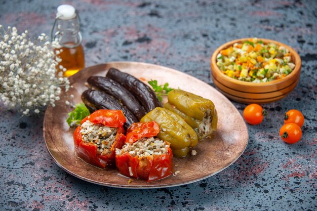 front view eggplant dolma with cooked tomatoes and bell-peppers filled with ground meat inside plate on blue background