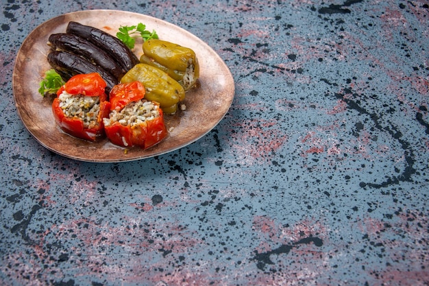 Vista frontale dolma di melanzane con pomodori cotti e peperoni ripieni di carne macinata all'interno della piastra su sfondo blu