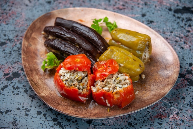 Foto gratuita vista frontale dolma di melanzane con pomodori cotti e peperoni ripieni di carne macinata all'interno della piastra su sfondo blu