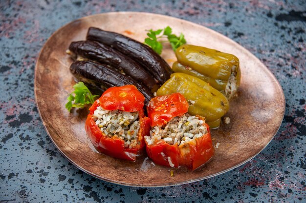 front view eggplant dolma with cooked tomatoes and bell-peppers filled with ground meat inside plate on blue background