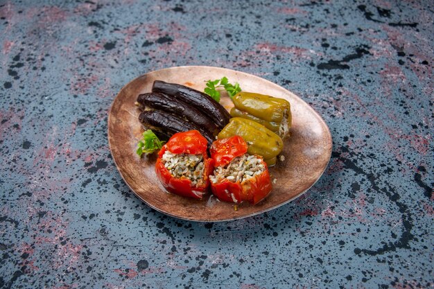 青の背景のプレートの内側にひき肉で満たされた調理済みトマトとピーマンの正面図ナスドルマ