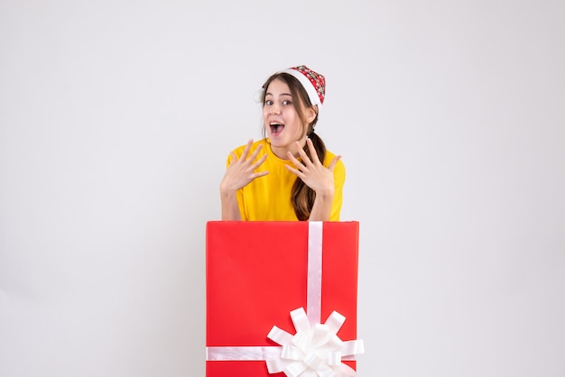 Front view elated girl with santa hat standing behind big xmas gift