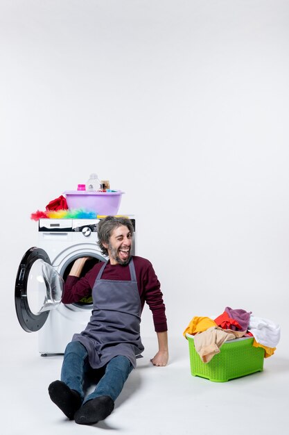 Front view elated male housekeeper putting hand in washer laundry basket on white background