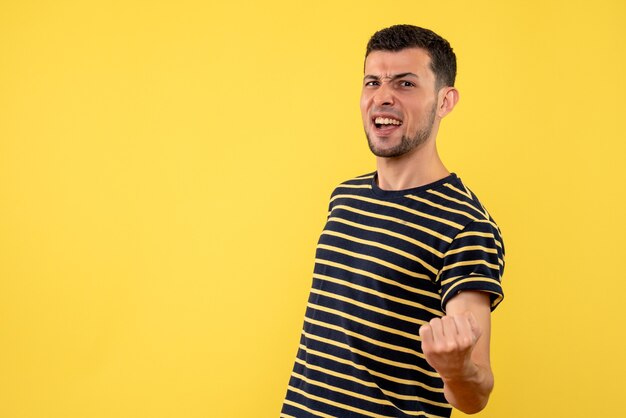 Front view elated young man in black and white striped t-shirt yellow isolated background