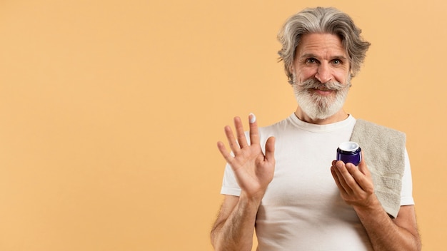 Front view of elder bearded man holding moisturizer
