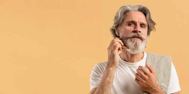 Free photo front view of elder man combing beard with copy space