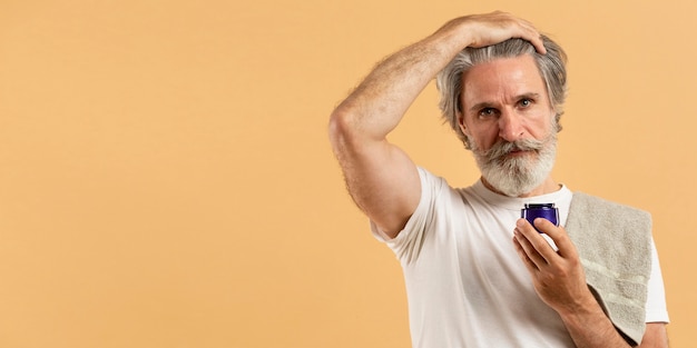 Free photo front view of elder man with beard holding moisturizer