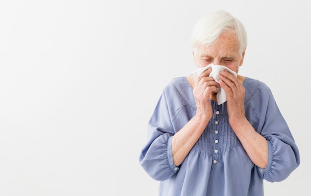 Front view of elder woman blowing her nose with copy space