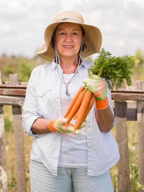 Front view elder woman holding some fresh carrots in her hand