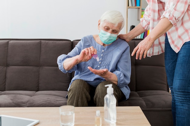 Free photo front view of elder woman using hand sanitizer while wearing medical mask