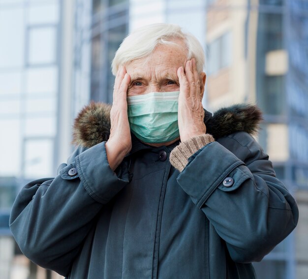 Front view of elder woman using medical mask while in the city