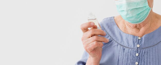 Front view of elder woman wearing medical mask and holding hand sanitizer