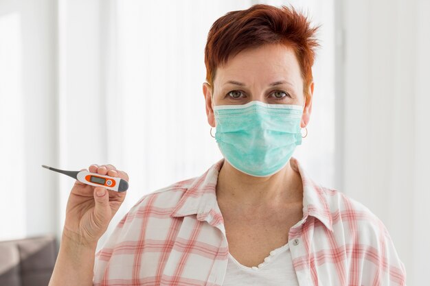 Front view of elder woman with medical mask holding thermometer