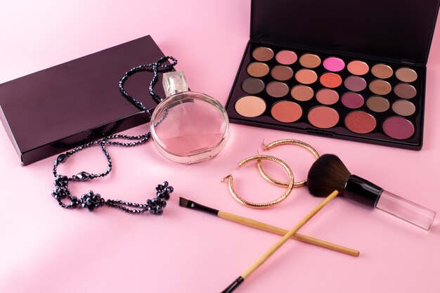 ピンクの机の上にネックレスと黒の化粧品ボックスが付いたエレガントな香りの正面図