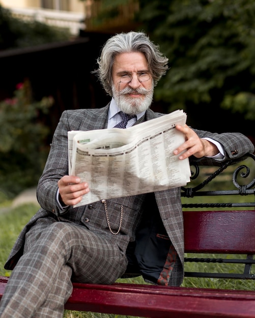 Бесплатное фото Вид спереди элегантный старший мужчина читает газету