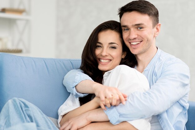 Front view of embraced smiley couple on sofa