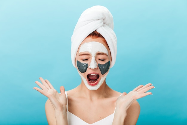 Free photo front view of emotional girl screaming while doing skincare treatment. studio shot of amazing lady with face mask isolated on blue background.