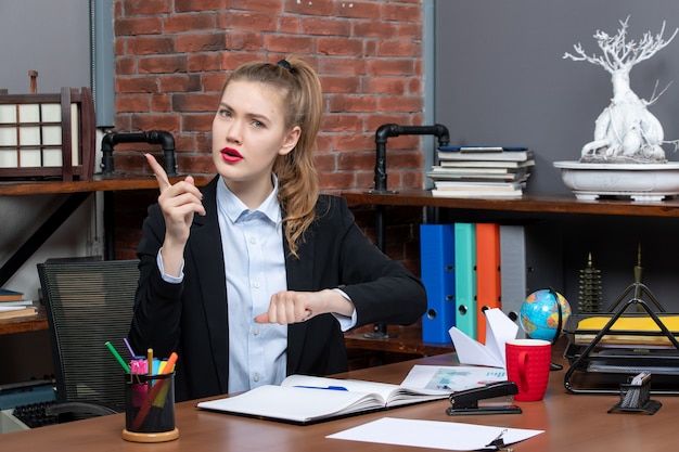 Front view of emotional shocked female sitting at a table and pointing up in the office