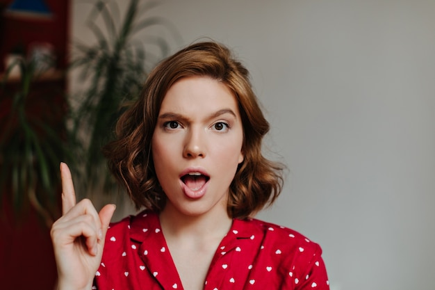 Front view of emotional woman in sleepwear showing idea sign. indoor shot of curly woman in red pajama gesturing at home.