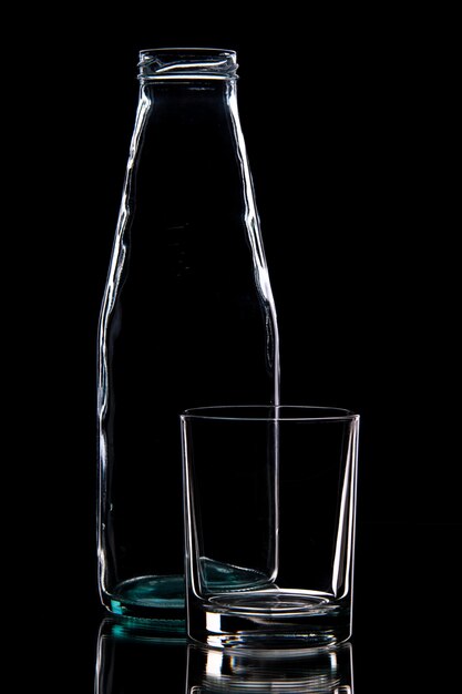 Вид спереди пустой бутылки и стакана на черном фоне со свободным пространством