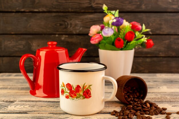 Front view of empty cup with red kettle brown coffee seeds and flowers on the wooden desk