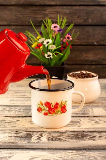 Front view of empty cup with red kettle brown coffee seeds and flowers on the wooden desk