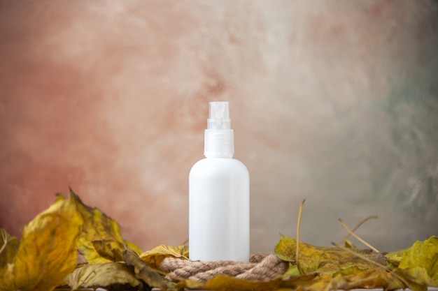 Free photo front view empty spray bottle around fall leaves on nude background