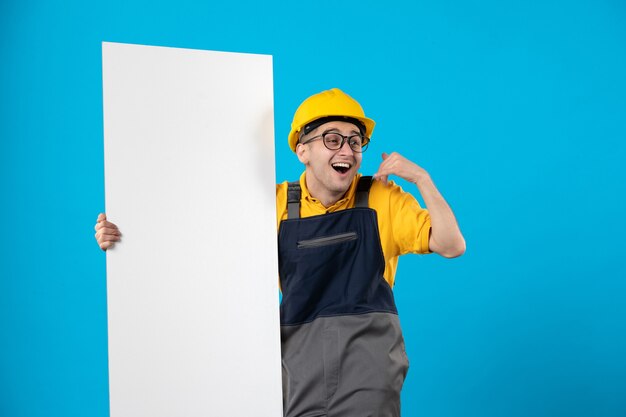 Вид спереди взволнованный мужчина-строитель в форме с бумажным планом на синем
