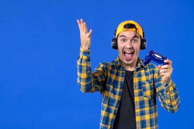 Front view of excited male gamer with gamepad playing video game on blue wall