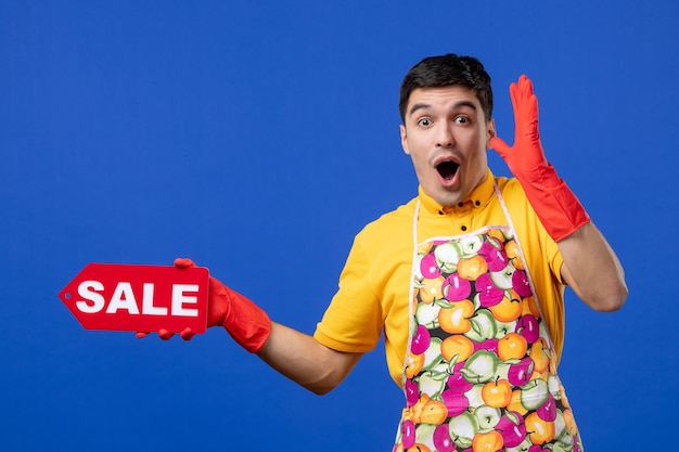Вид спереди возбужденный мужчина-экономка в желтой футболке держит знак продажи на синем пространстве
