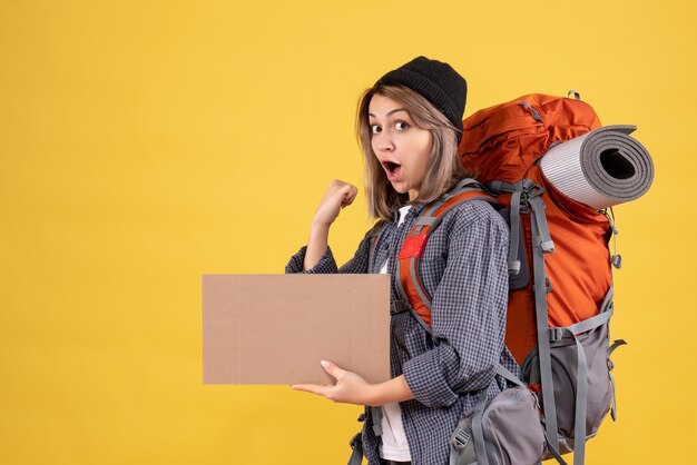 Front view of excited traveler woman with backpack holding cardboard