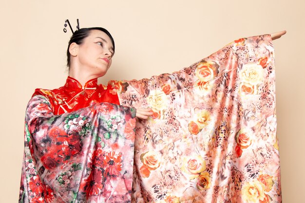 A front view exquisite japanese geisha in traditional red japanese dress posing with flower designed tissue elegant on the cream background ceremony japan