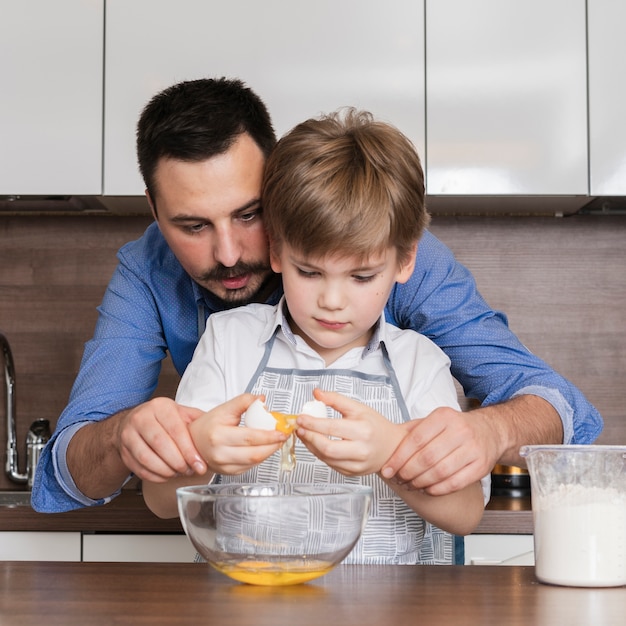 Front view father helping son to crack eggs