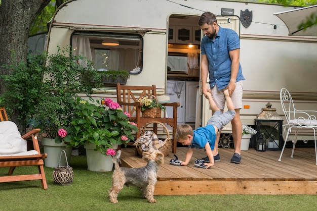 Front view father playing with his son next to a caravan