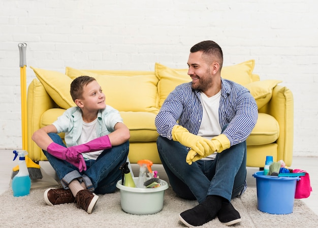 Vista frontale del padre e del figlio che riposano accanto ai prodotti per la pulizia