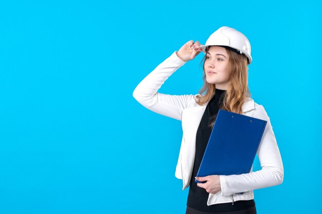 Front view female architect in helmet holding blue file plan on blue