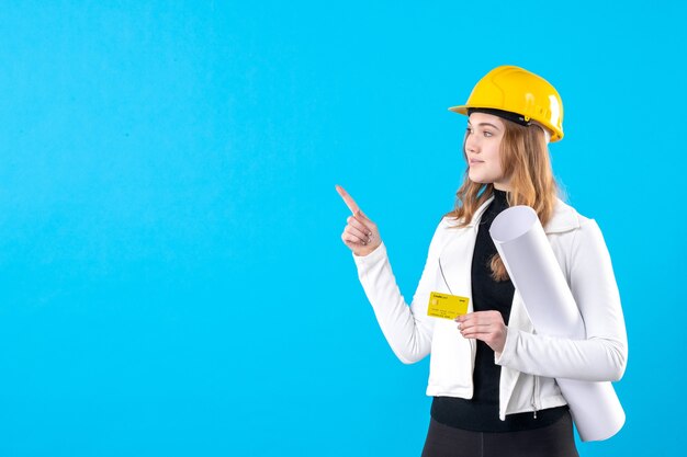 Front view female architect holding plan and bank card on blue