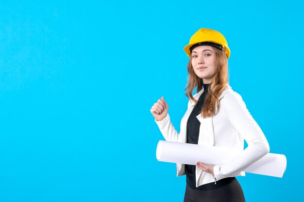 Front view female architect in yellow helmet holding plan on blue