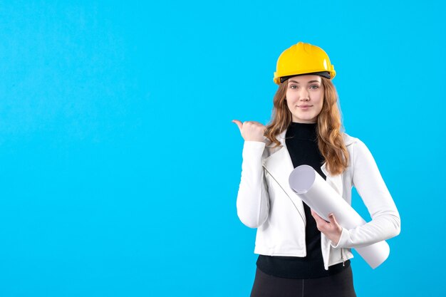 Front view female architect in yellow helmet holding plan on blue