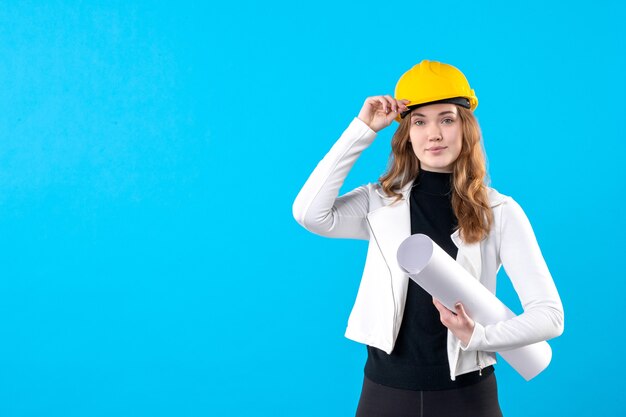 Front view female architect in yellow helmet holding plan on blue