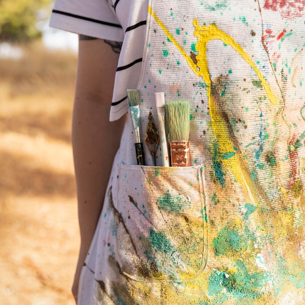 Free photo front view of female artist with apron full of paint and brushes