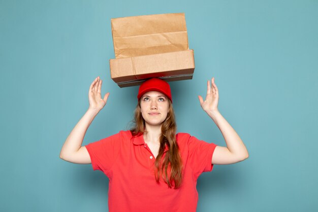 Free photo a front view female attractive courier in red polo shirt red cap holding brown packages above her head posing on the blue background food service job