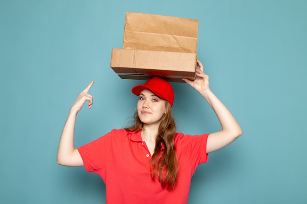 Foto gratuita un corriere attraente femminile di vista frontale in spiritello malevolo rosso della camicia di polo che tiene i pacchetti marroni che posano sorridente sul lavoro blu di servizio ristoro del fondo