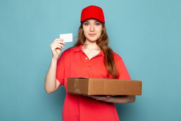 빨간 폴로 셔츠 빨간 모자와 청바지 파란색 배경 음식 서비스 작업에 웃 고 포즈 상자를 들고 전면보기 여성 매력적인 택배