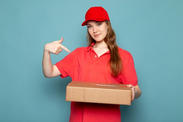 빨간 폴로 셔츠 빨간 모자와 청바지 파란색 배경 음식 서비스 작업에 웃 고 포즈 패키지를 들고 전면보기 여성 매력적인 택배