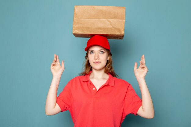 Foto gratuita un corriere attraente femminile di vista frontale in spiritello malevolo rosso che sorride posando il pacchetto della tenuta sopra la sua testa sul lavoro blu di servizio ristoro del fondo