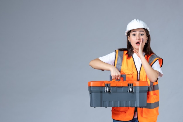 Vista frontale del costruttore femminile che porta una valigetta per attrezzi pesante sul muro bianco